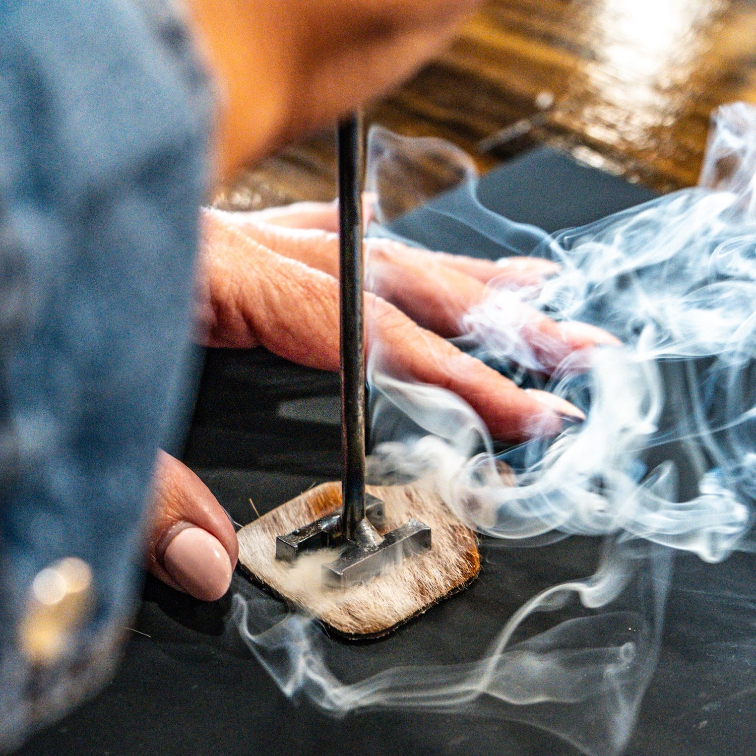 Person branding a cowhide keychain with smoke rising.